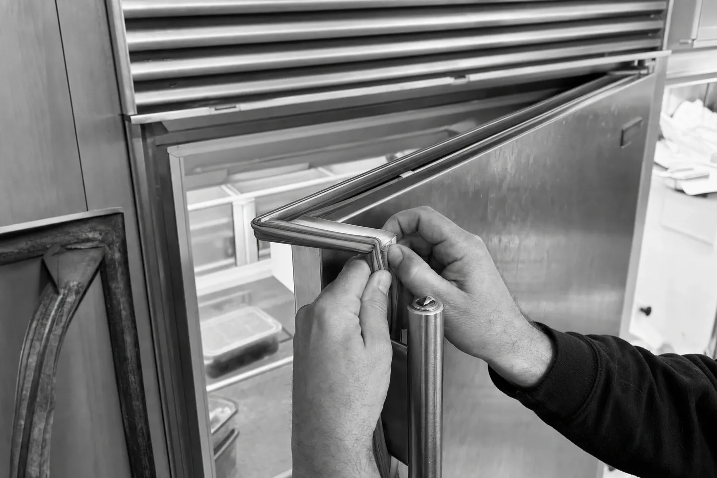 Black-and-white frame of hands seating a gasket into the door frame of a large stainless built-in