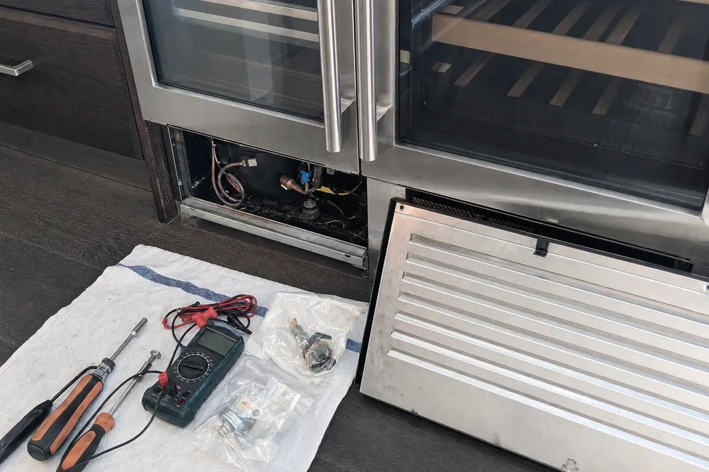 Grille panel lifted off and leaning on the floor beside an open machine bay, tools laid out on a white cloth